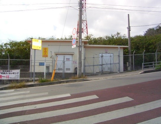 道路を渡った先のライトの付いた看板と柵の中の肌色の壁の建物の写真