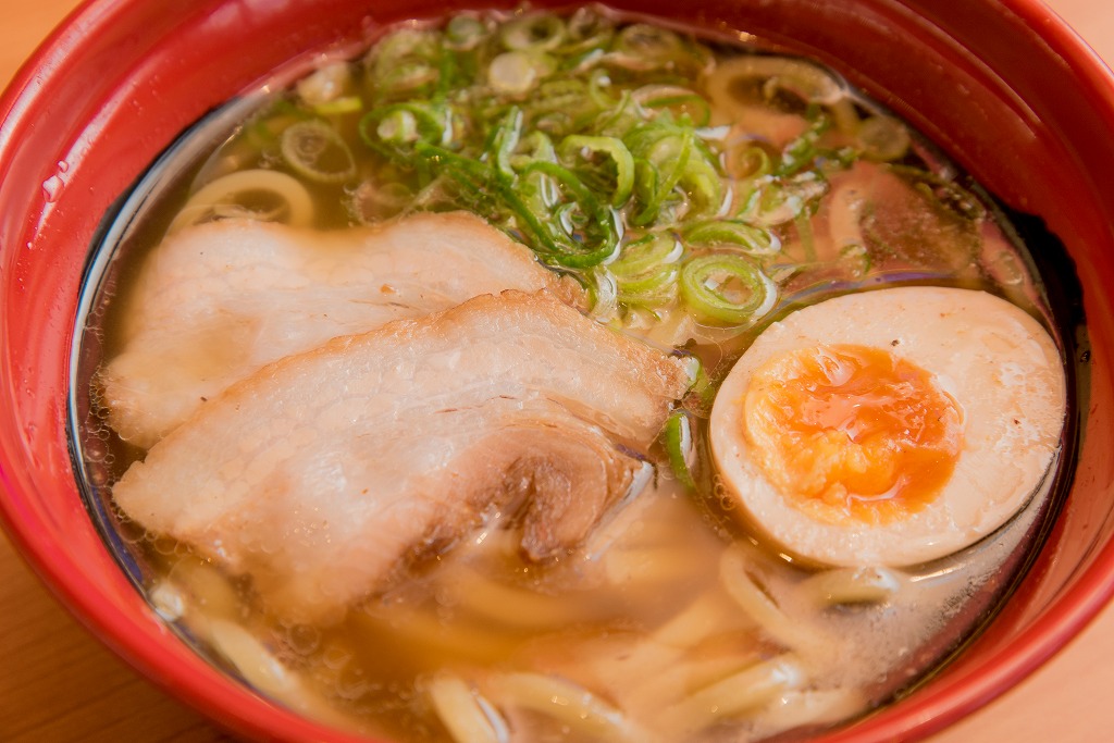 赤いお椀に入った2切れの肉と卵、ネギの載った麺類の写真