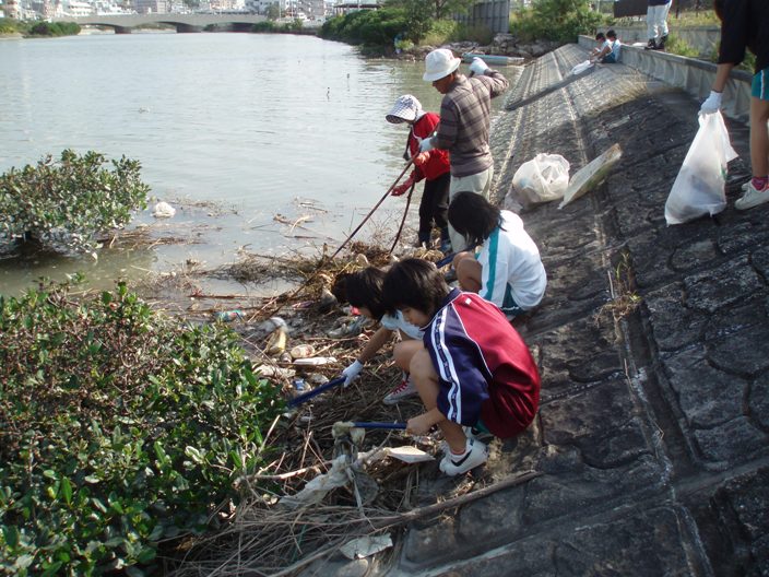 漫湖の堤防に流されてきたゴミを集めている学生や近隣住民の清掃活動の写真
