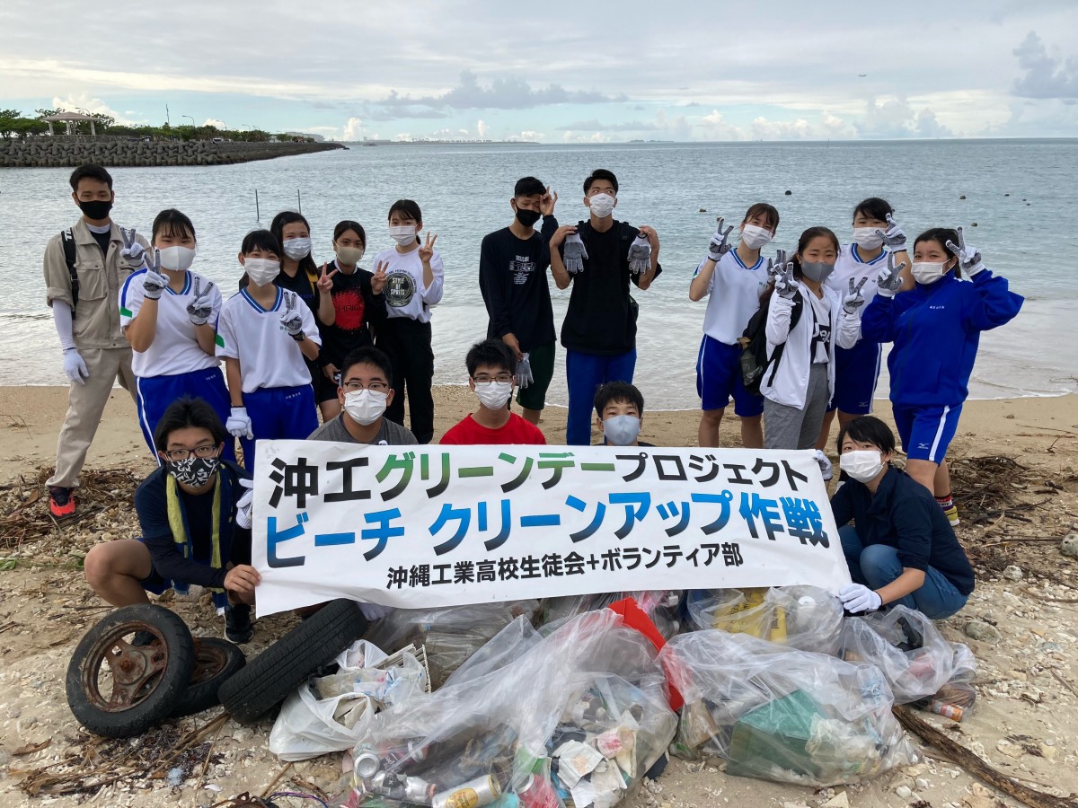 沖縄工業高校生徒会とボランティア部の人たちがゴミ袋を前に横断幕を掲げている写真