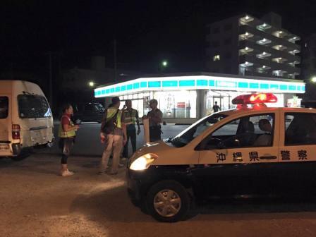 夜中のコンビニの前にパトカーが止まっており警察官と反射板のついた安全服を着た人達が会話をしている写真