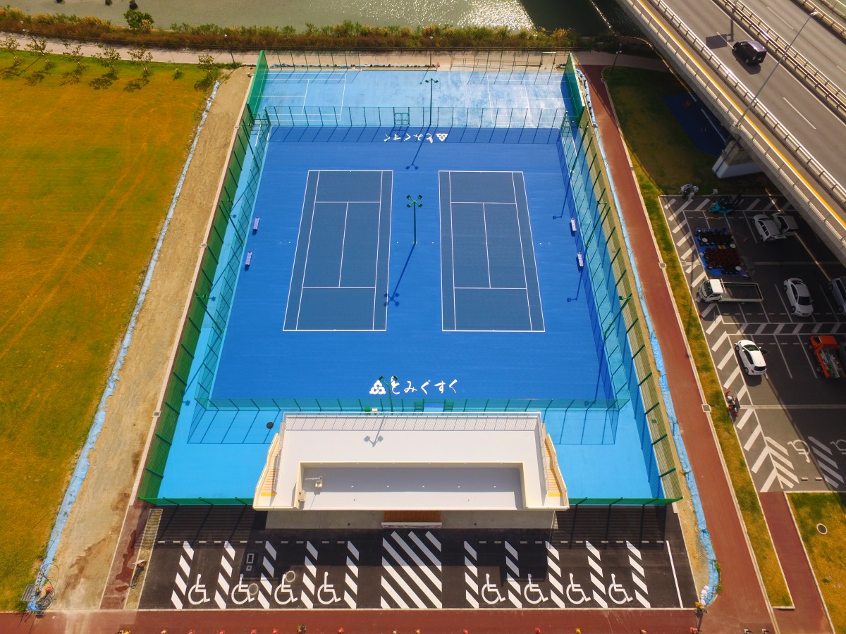 緑の柵で囲まれた青い地面の2面あるテニスコートを上から写した写真
