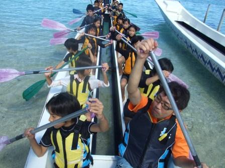 海でボートに複数の子供が乗りパドルを持って漕いでいる写真