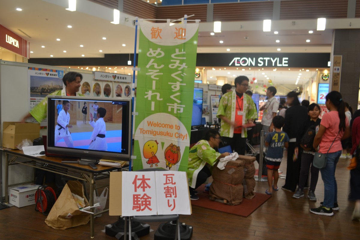 屋内で瓦割り体験と書かれた看板の後ろで法被を着た複数の男性の前に複数の人が並んでいる写真