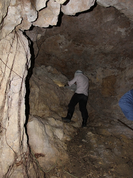 岩をくりぬいたような洞窟の中に、懐中電灯を持った人が立っている写真