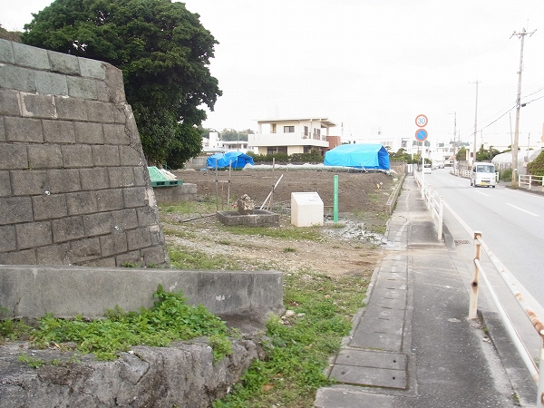 車道の横の敷地に、小さな石像と台座と案内表示が並べて置かれている写真