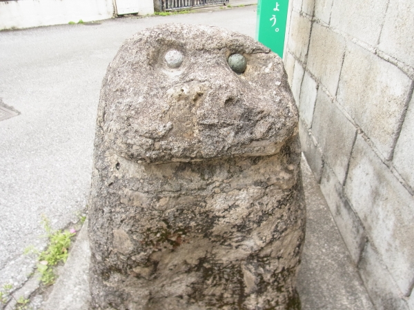 丸い目が印象的な、つるつるした体つきのシーサーの石像の顔部分を撮影した写真