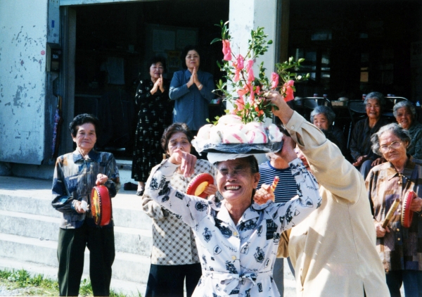 笑顔の女性が、木の飾りなどが乗ったお盆を頭の上にのせている写真