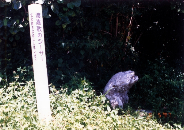「渡嘉敷のシーサー」と書かれた標識の奥に、石の置物が置かれている写真