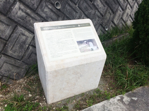 石の壁の前に、白い台座があり、字宜保のビジュンの説明文が書かれている写真
