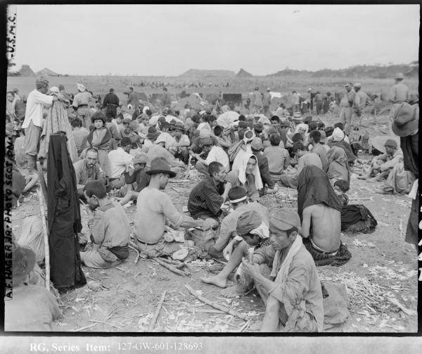 ボロボロの服を着た人たちが、地面に座り込んでいる白黒写真