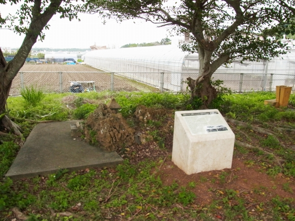 畑とビニールハウスを背にした場所に、白い台座が置かれている写真