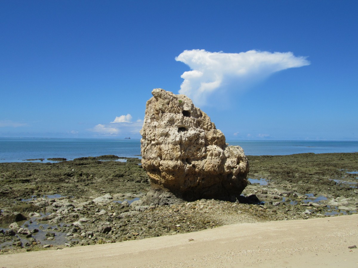 晴れた空の海岸に小さい穴が空いた大きな岩の塊がある写真