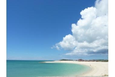 右に大きな雲のある青空と、弓形に広がる砂浜と海の写真(オリオンECO美らSUNビーチ とみぐすく観光ガイドへリンク)