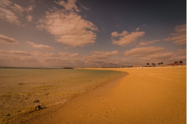 夕日でうっすら赤くなった弓形の砂浜と海の写真(オリオンECO美らSUNビーチ サンセット とみぐすく観光ガイドへリンク)