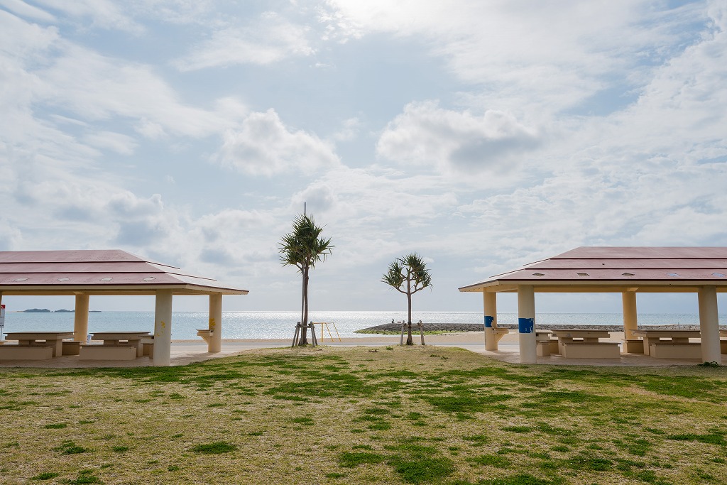 海辺に面した屋根付きの休憩所と合間に生える木々の写真