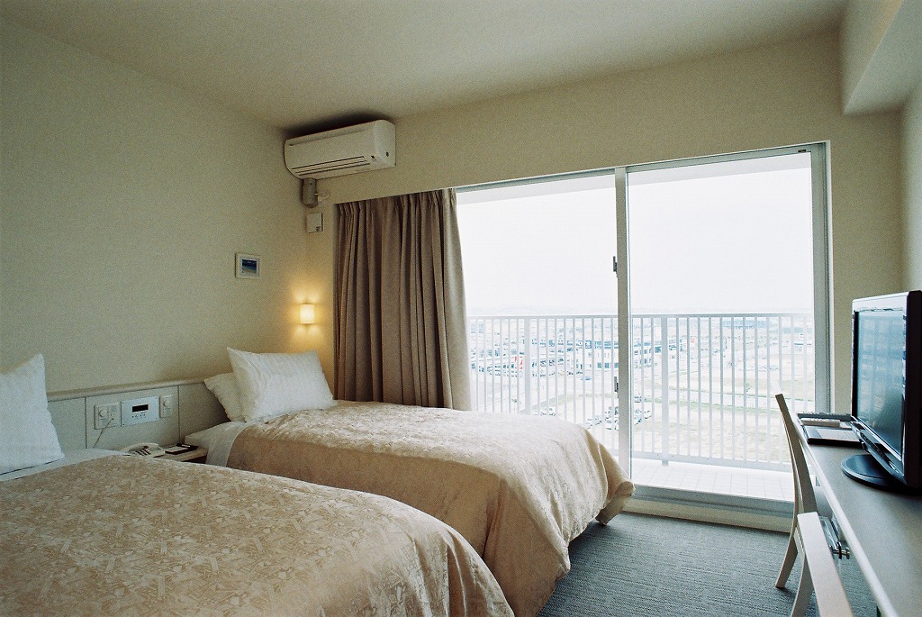 ベッドが2つあり、外が見晴らせるベランダ付きの客室の写真