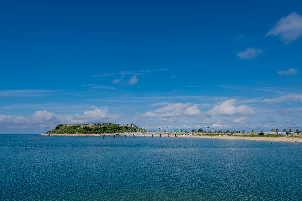 青い空と青い海、そこに浮かぶ緑の丘と横に伸びる海岸の写真