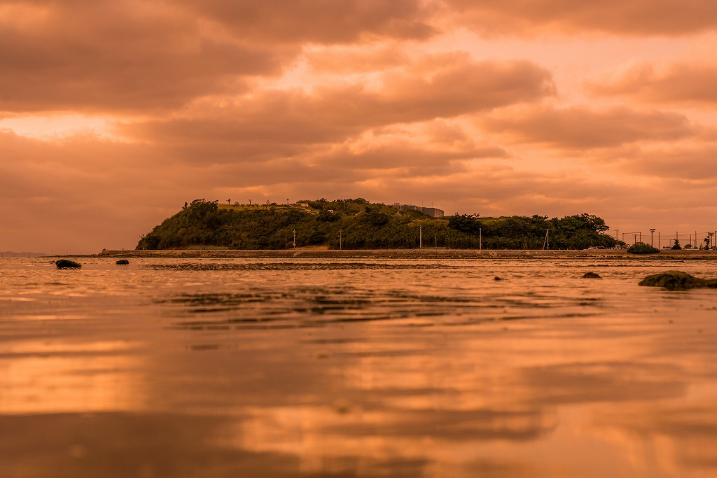 夕日で赤く染まった空と海面と瀬長島の写真