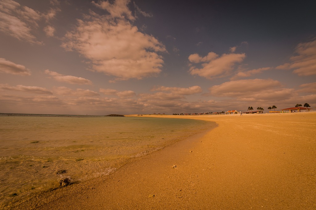 夕日で赤く染まった弓形の砂浜と海の写真
