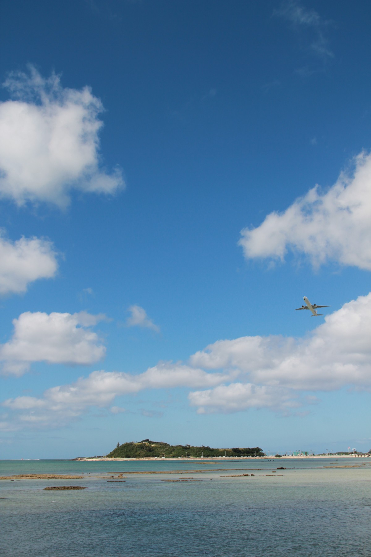 青空の海に浮かぶ小島と空を飛ぶ飛行機の写真