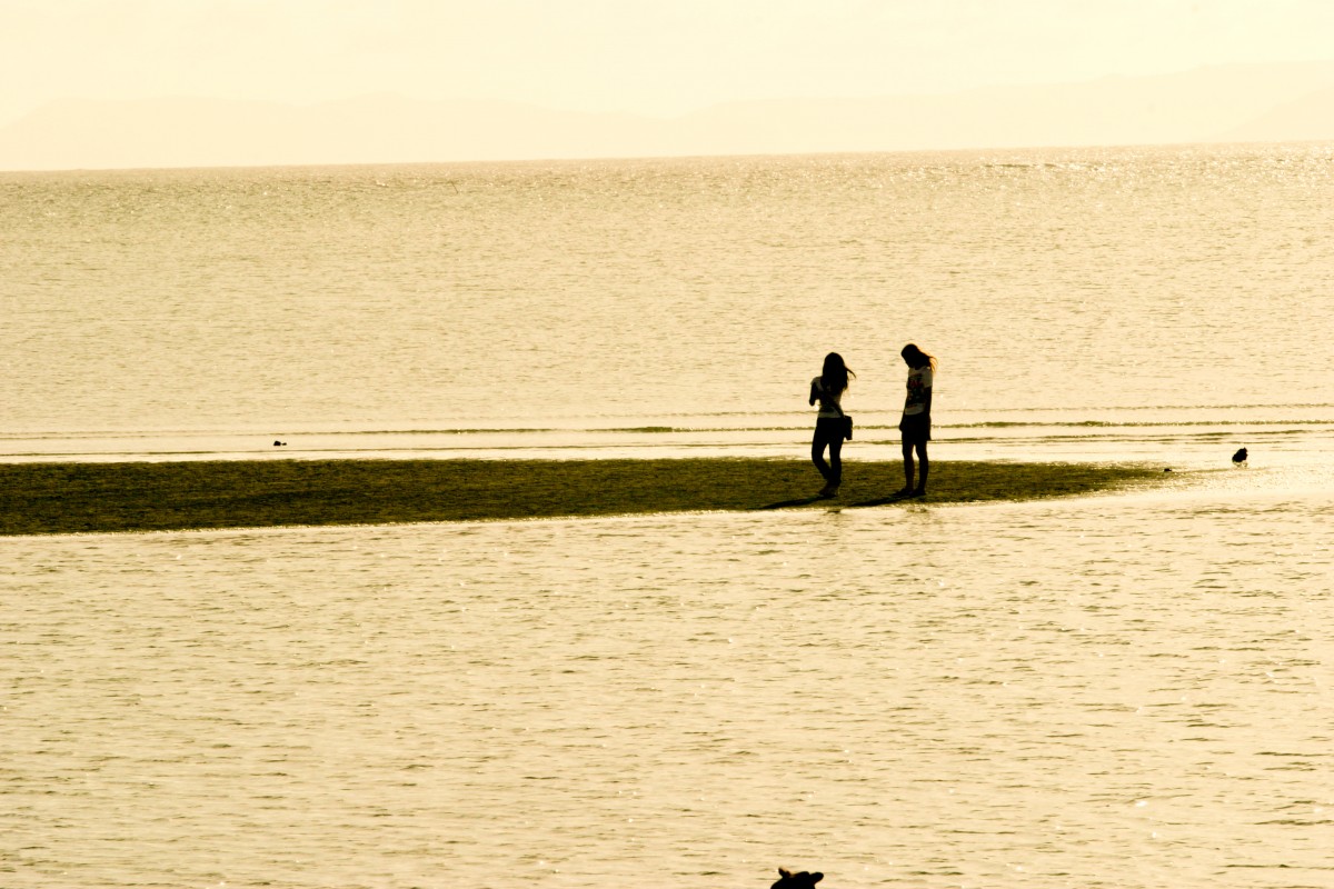 薄暗い砂浜の上に2人の女性が立っている姿が影になった写真