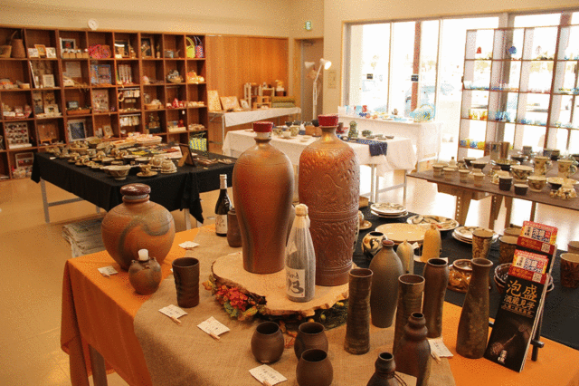 棚や机に置かれた複数の湯飲みや花瓶や坪やマグカップが売られている店内の写真